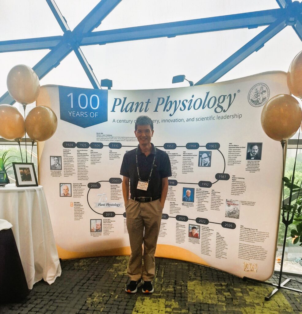 Yunde Zhao stands in front of decorative display for Plant Physiology. 